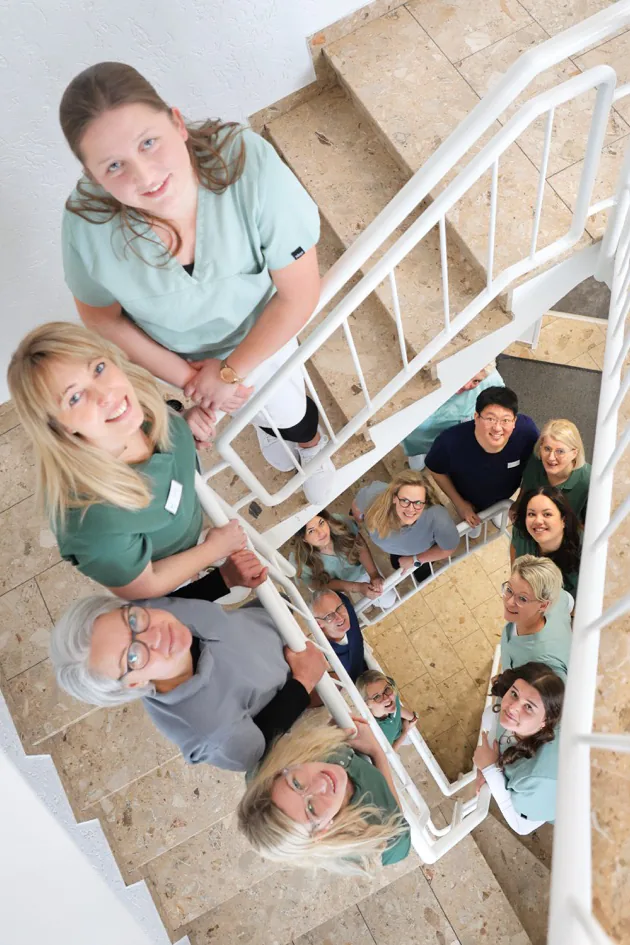 Das Zahngut-Team lächelt gemeinsam im hellen Treppenhaus in die Kamera.